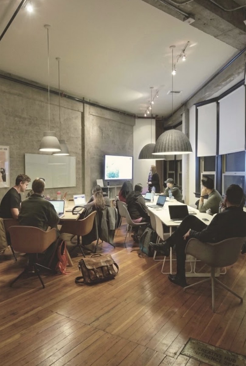 A group with laptops in a loft office, a presentation on the wall at the front