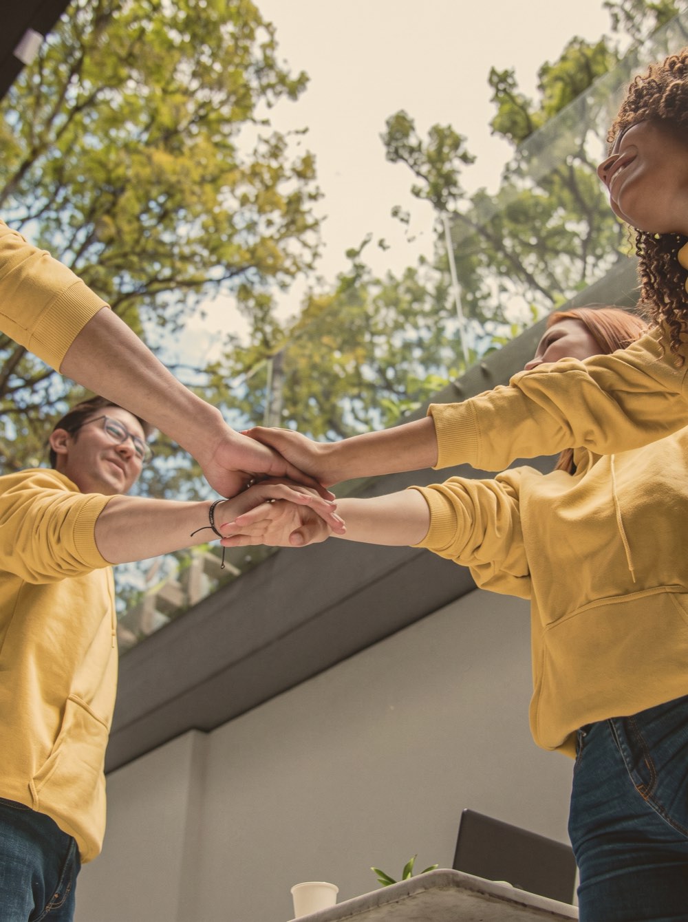Three people in yellow hoodies putting their hands together