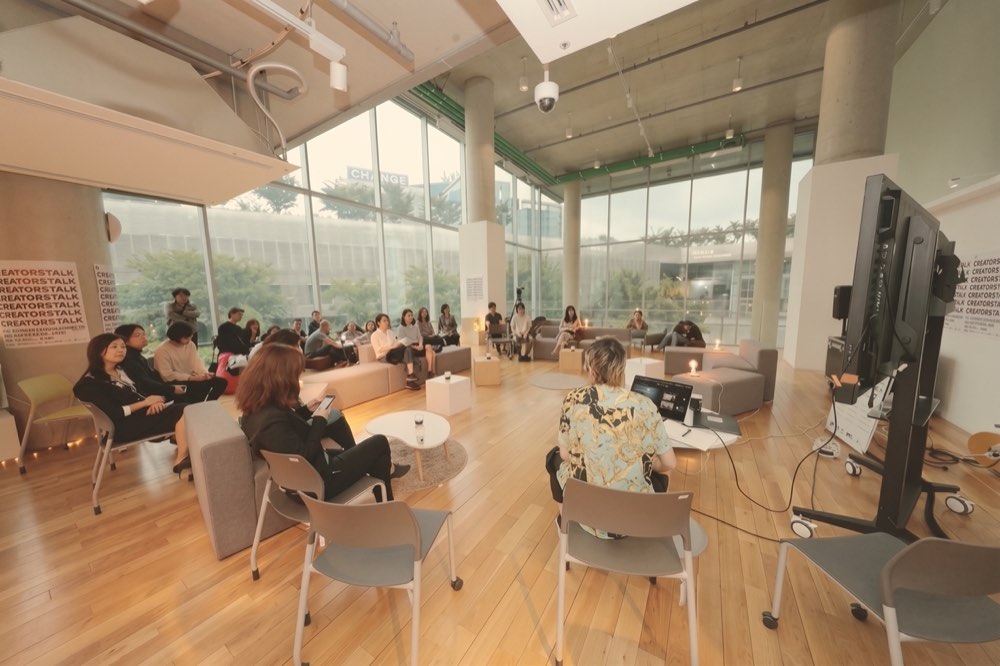 A group in a bright room with a glass front, facing a large screen: a talk with an audience